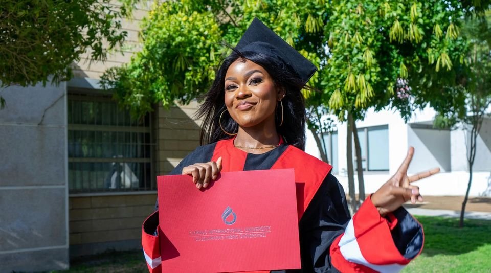 Jeune diplômée en toge rouge et noire, souriante, tenant son diplôme à l’extérieur