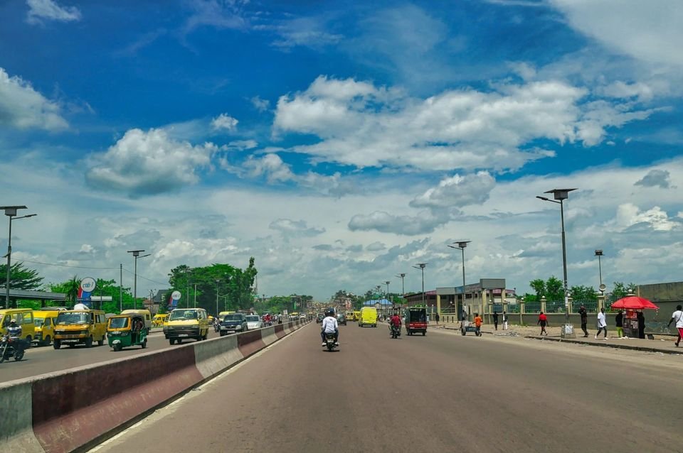 Large avenue urbaine bordée de lampadaires, avec circulation et ciel nuageux